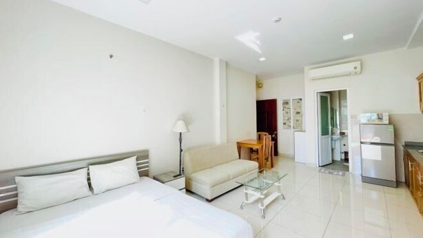 A hotel room with a bed, a sofa, a small table, a lamp, a kitchenette, and a bathroom. - EMERALD APARTMENT (Ho Chi Minh City)