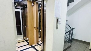 A hallway with a wooden door, a glass elevator door, and a staircase with a metal railing. - EMERALD APARTMENT (Ho Chi Minh City)