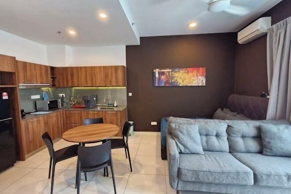 A modern kitchen with wooden cabinets, a dining table with chairs, a grey sofa, and a colorful abstract painting on the wall. - H&W Sunway Onsen Suite S-07-05 near Lost World of Tambun Ipoh (Ulu Kinta)