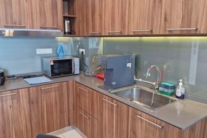 Una cocina moderna con armarios de madera, un lavamanos de acero inoxidable, un microondas y una cafetera.