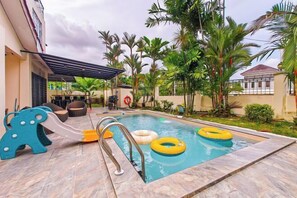 A swimming pool with a slide, surrounded by palm trees and a covered seating area. - JB Town Villa by RR JBcity (Johor Bahru)
