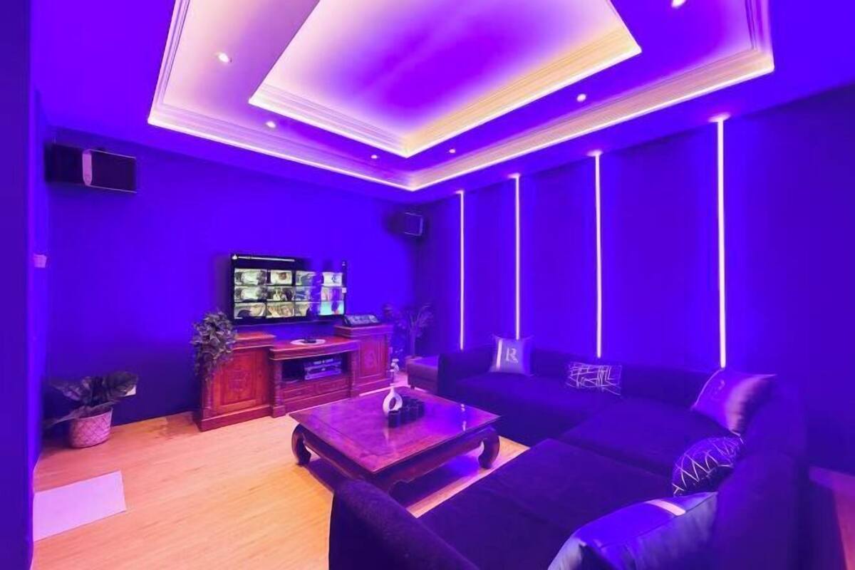 Une pièce avec un mur bleu foncé, un téléviseur à écran plat, une table basse en bois, un canapé noir et un plafond doté d’un éclairage encastré.