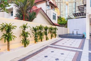 Un cortile con pavimento in piastrelle, un muro bianco con piante e un edificio con tetto rosso sullo sfondo.
