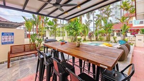 A covered outdoor dining area with a pool, wooden table, chairs, and a ceiling fan. - JB Town Villa by RR JBcity (Johor Bahru)