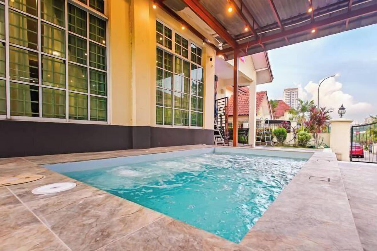 Une piscine avec une terrasse carrelée, un espace couvert doté d’un toit et un bâtiment avec de grandes fenêtres.