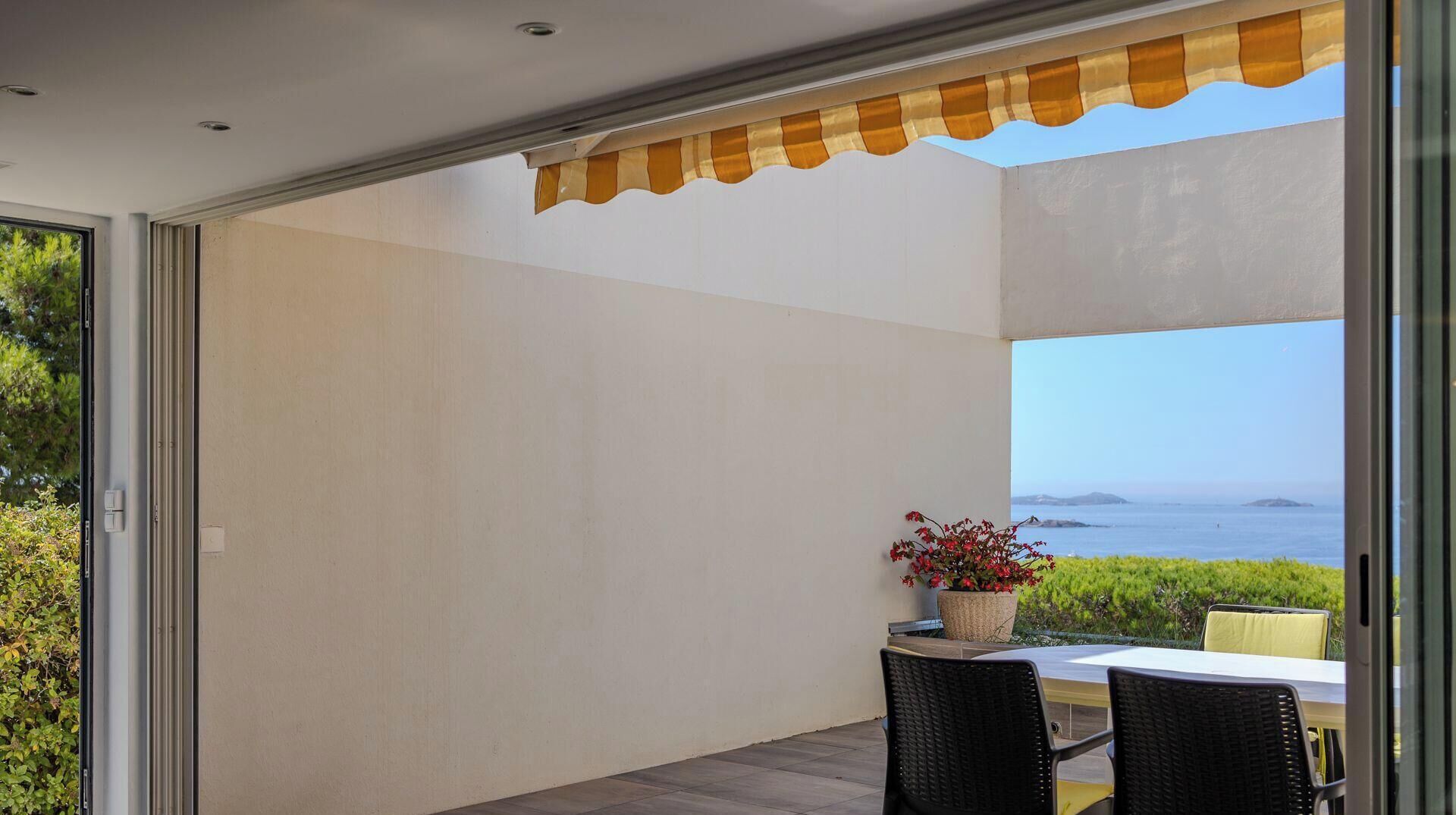 Eine moderne Terrasse mit Tisch und Stühlen, einem Blumentopf und Blick aufs Meer.