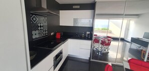A modern kitchen with a black countertop, white cabinets, and a patterned backsplash. There is a red chair and a table outside the kitchen window.