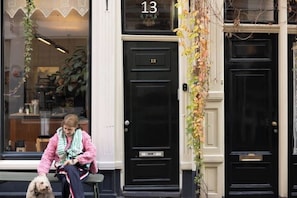Henkilö istuu penkillä rakennuksen ulkopuolella. Rakennuksessa on musta ovi, jonka yläpuolella on numero 13.