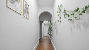 A narrow hallway with wooden flooring, white walls, and a white door at the end. - Huge Home | Sleeps 10+ | Minutes from NYC (Bayonne)