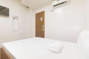 Habitación de hotel con cama, puerta de madera, aire acondicionado instalado en la pared y un espejo.