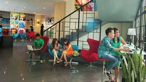 Um lobby moderno com escadaria, áreas de estar coloridas e uma pessoa usando um laptop.
