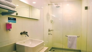 Casa de banho com cabine de chuveiro envidraçada, lavatório branco e espelho em cima.