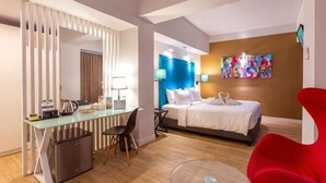Quarto de hotel com cama, escrivaninha, cadeira e televisão.