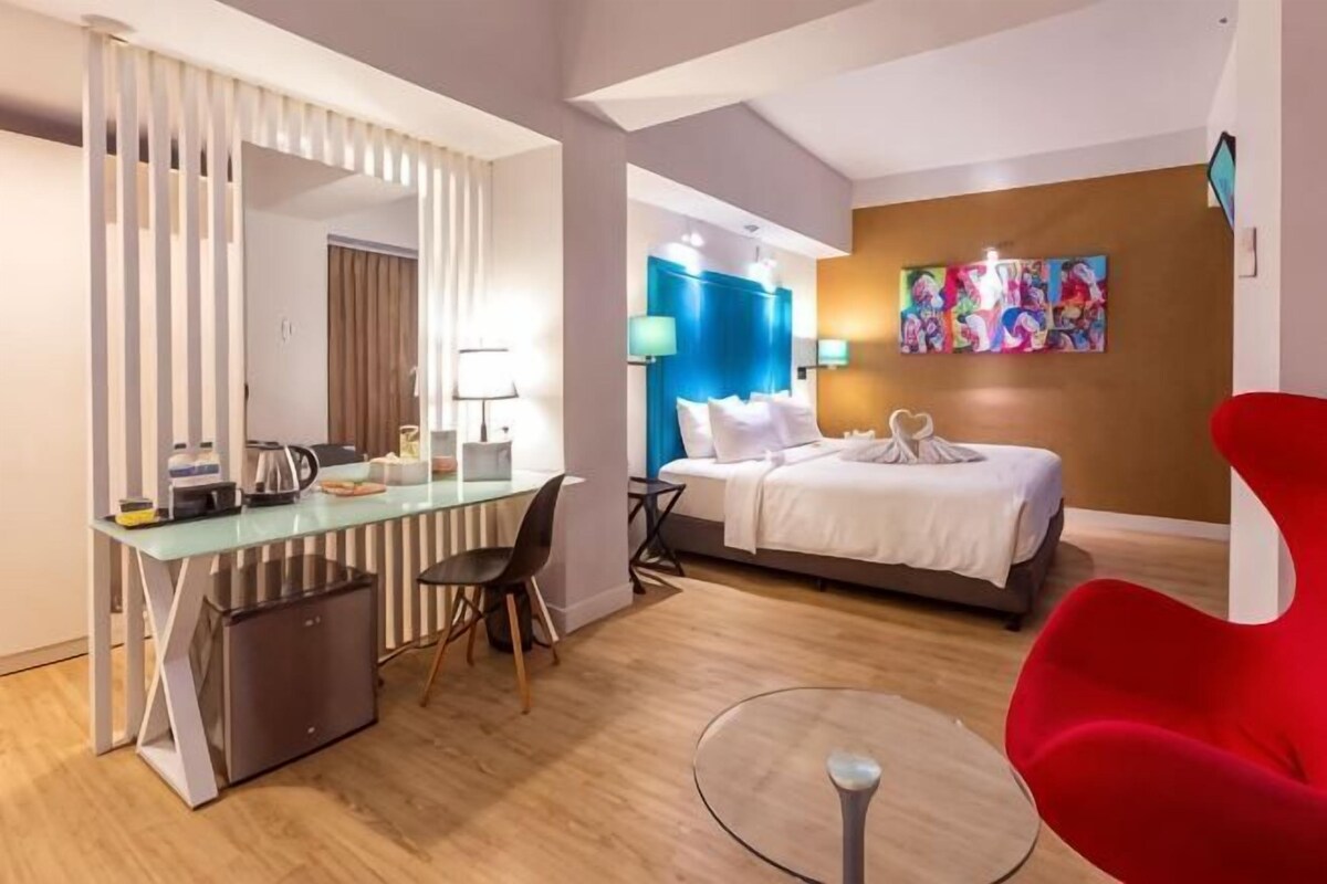 A hotel room with a bed, desk, chair, and a TV.