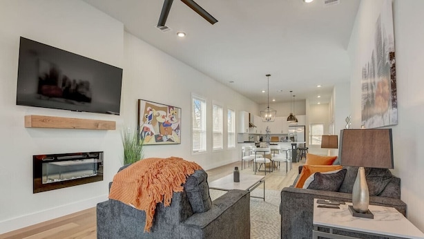 Una sala de estar moderna con chimenea, televisor y comedor, con una cocina al fondo.