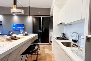 A modern kitchen with a marble countertop, black chairs, a TV, and a sliding glass door leading to a balcony. - Chambers Residence by Manhattan Group (Kuala Lumpur)