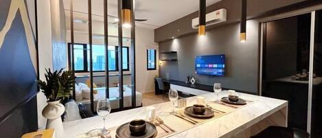 Una cocina moderna con encimera de mármol, sillas negras y un televisor de pantalla plana montado en la pared.