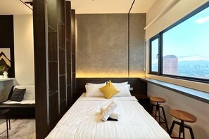 A modern hotel room with a bed, a sofa, a window with a city view, and a bar area. - Chambers Residence by Manhattan Group (Kuala Lumpur)