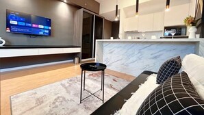 A modern living room with a flat-screen TV, a sofa, a small black table, and a kitchen area with a marble countertop. - Chambers Residence by Manhattan Group (Kuala Lumpur)