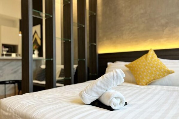 A neatly made bed with a rolled towel, a yellow pillow, and a headboard.