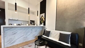 A modern kitchen with a marble countertop, black sofa, and pendant lighting. - Chambers Residence by Manhattan Group (Kuala Lumpur)