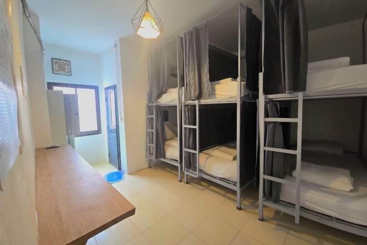 A dormitory room with bunk beds, a wooden table, and a window.