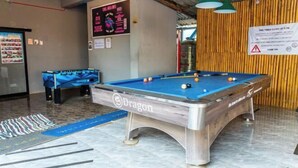 A pool table with a blue felt surface and a Dragon logo, a smaller pool table in the background, and a sign indicating pool table closure times. - Vang Vieng Chill House (Vang Vieng)
