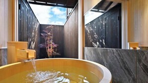 Una bañera de madera con agua corriendo, frente a paneles de madera oscura y una vista del cielo.