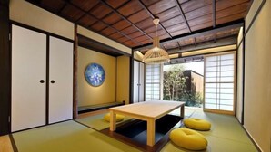 Una habitación tradicional japonesa con suelo de tatami, una mesa baja de madera, puertas correderas y una lámpara colgante.
