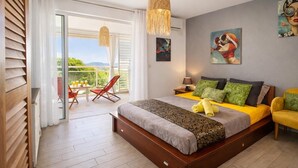 A bedroom with a large bed, a balcony with a table and chairs, and artwork on the walls. - Les Alizés Joli Studio sea view beach walk Anse Mitan Trois ILETS (Trois Ilets)