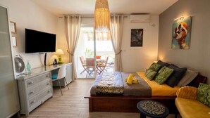 A hotel room with a bed, a desk, a TV, a balcony with a chair, and a painting on the wall. - Les Alizés Joli Studio sea view beach walk Anse Mitan Trois ILETS (Trois Ilets)