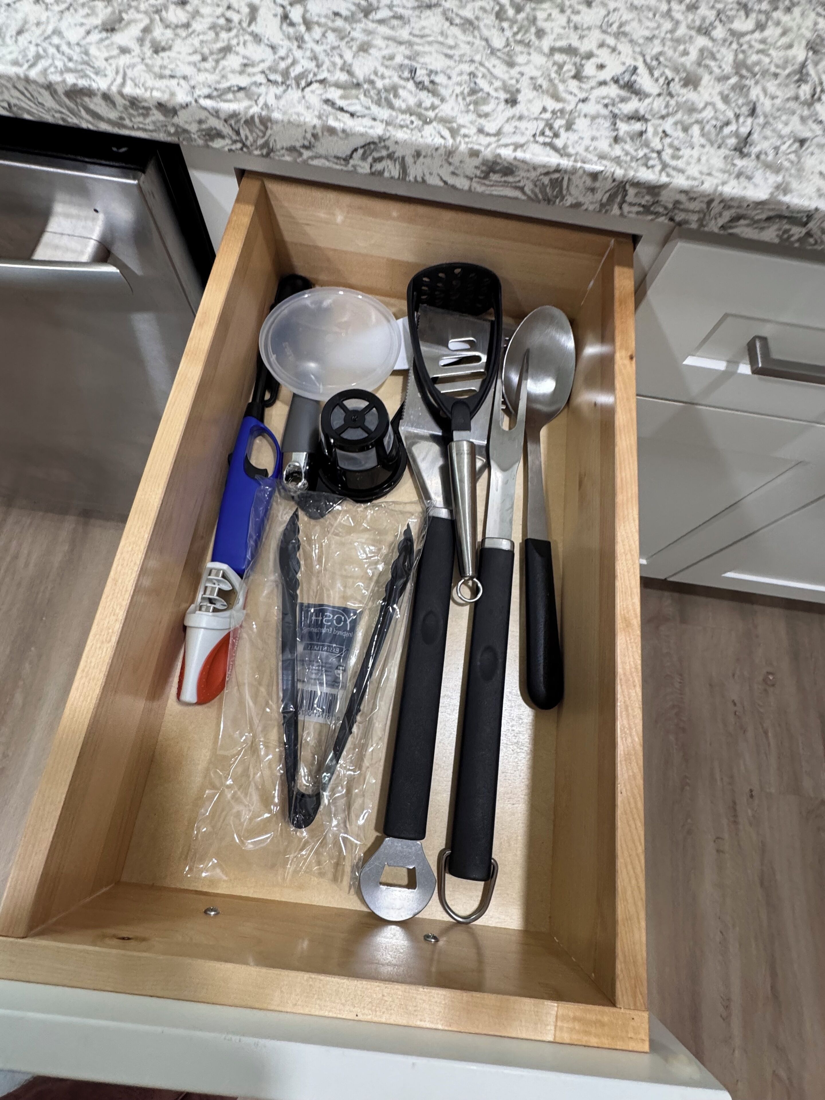 Un tiroir contenant des ustensiles de cuisine, notamment une spatule, une louche et des tasses à mesurer.