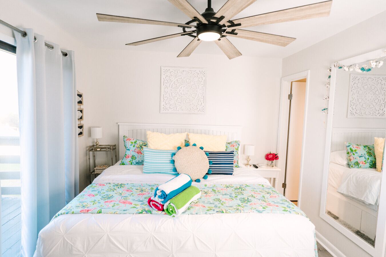 Quarto com cama, ventoinha no teto, mesa de cabeceira e espelho.