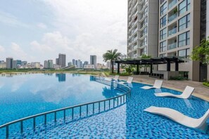 A swimming pool with lounge chairs, a city skyline in the background, and a high-rise building. - Flora Urban - Premium Apartment Vinhomes Skylake Near Keangnam (Hanoi)
