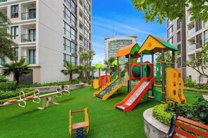 A playground with slides and swings, surrounded by greenery and buildings. - Flora Urban - Premium Apartment Vinhomes Skylake Near Keangnam (Hanoi)