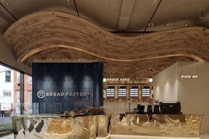 A modern interior with a curved wooden ceiling, a reception desk, and a sign that reads 'BREAD FACTORY'. - Flora Urban - Premium Apartment Vinhomes Skylake Near Keangnam (Hanoi)