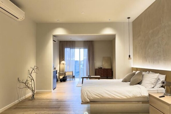 A hotel room with a large bed, bedside tables, a desk, and a chair. There is a view of the city through the window.