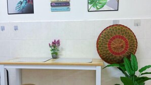 Una zona de cocina con encimera blanca, dos taburetes de madera, una cesta tejida y una planta en maceta.