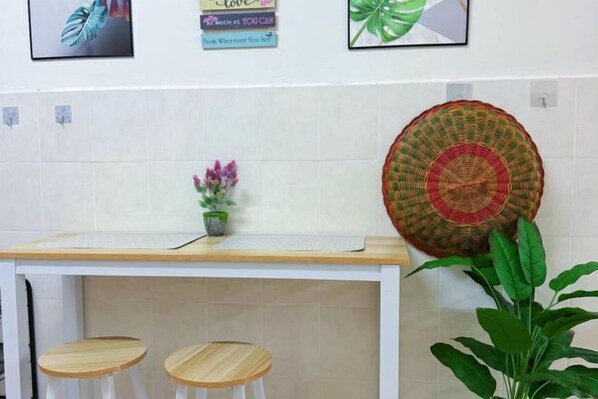 Una zona de cocina con encimera blanca, dos taburetes de madera, una cesta tejida y una planta en maceta.