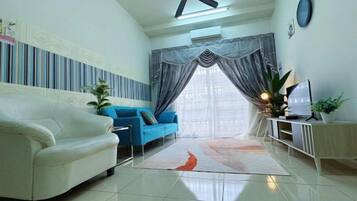 A living room with a white sofa, a blue sofa, a TV on a stand, and a ceiling fan.