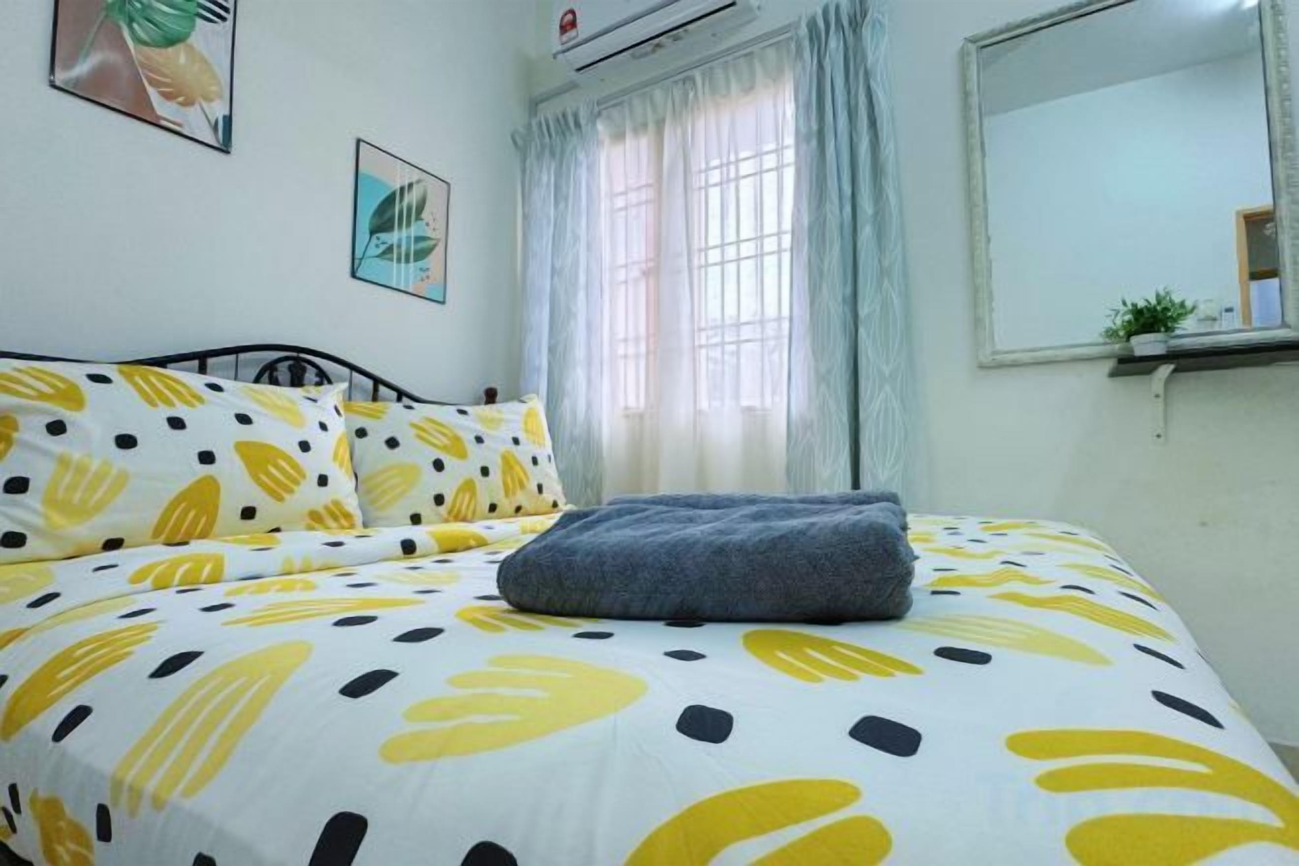 Una cama con una colcha estampada, una mesita de noche, una ventana con cortinas y un espejo fijado a la pared.