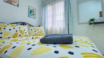 Una cama con una colcha estampada, una mesita de noche, una ventana con cortinas y un espejo fijado a la pared.