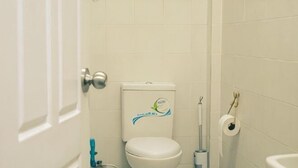 Un baño con inodoro, un rollo de papel higiénico y una botella azul de limpiador.