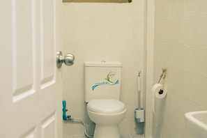 A bathroom with a toilet, a roll of toilet paper, and a blue cleaning spray bottle. - Happy Hope (Bangkok)