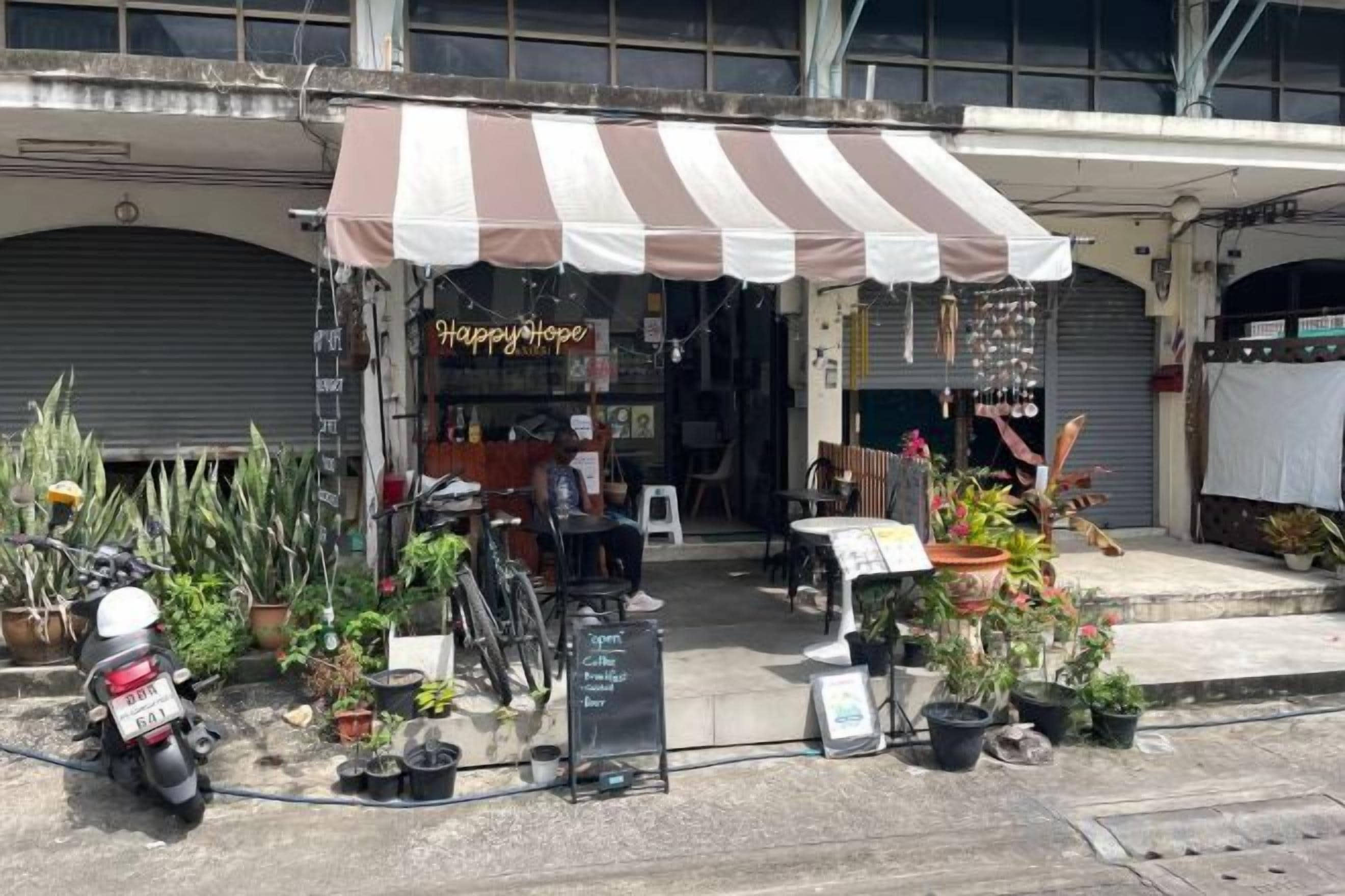 A storefront with a striped awning, potted plants, and a sign that reads 'Happy Hope.'