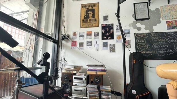 Una habitación con un escritorio desordenado, lleno de libros, CDs, una guitarra y un cartel de Harry Potter.