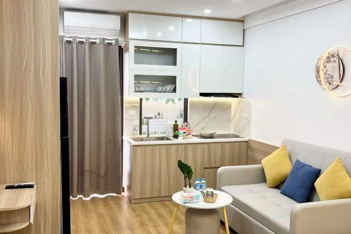 A modern living room with a sofa and a small round table, a kitchen area with cabinets and a countertop, and a wall-mounted decorative plate.