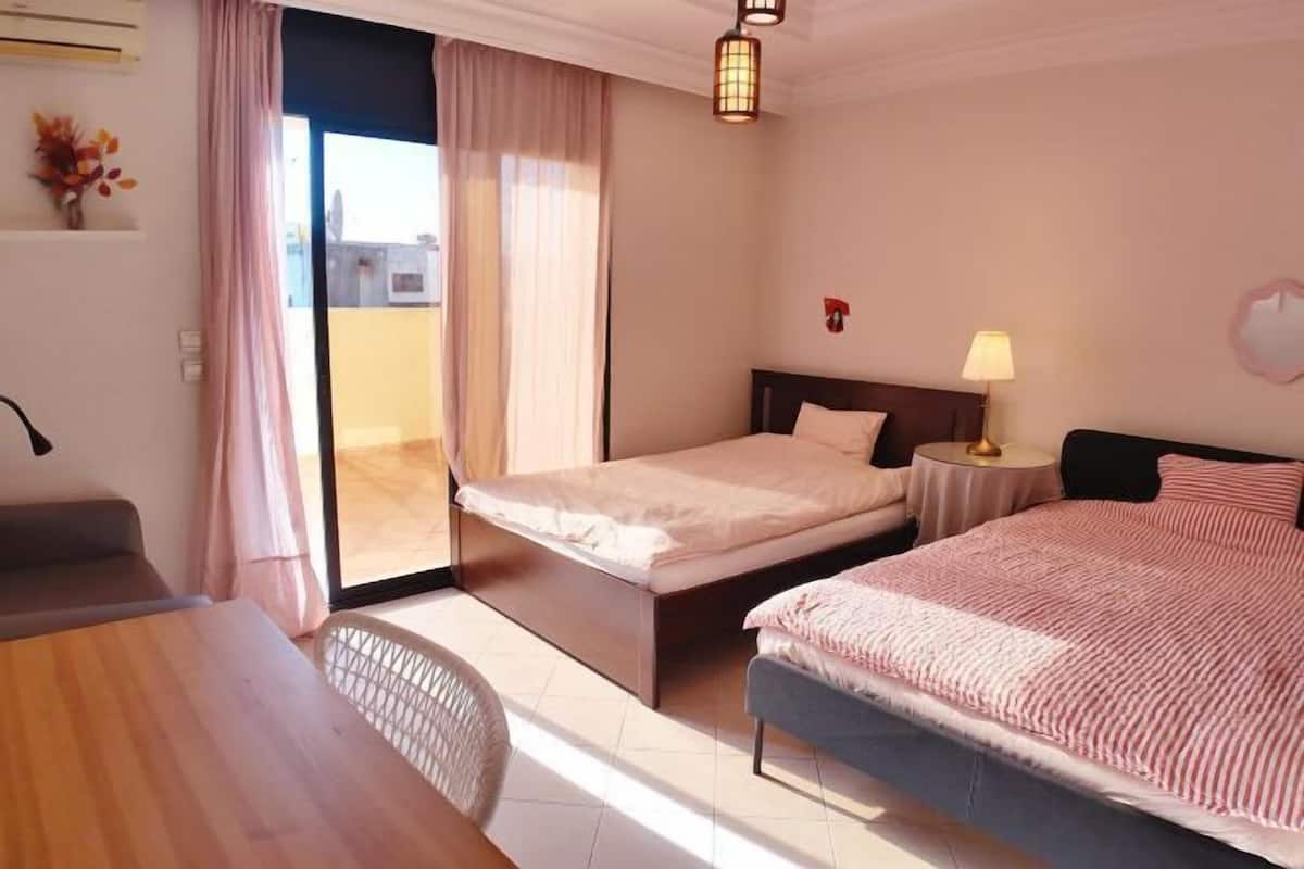A hotel room with a bed, a desk, a chair, a lamp, and a view through a glass door.