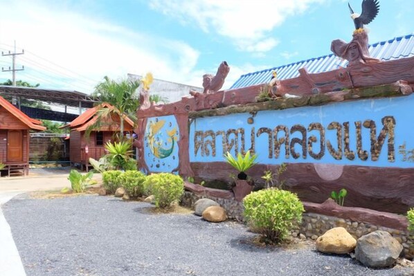 A sign with Thai script, surrounded by tropical plants and rocks. - Talad Nam Klong Hae Resort (Hat Yai)