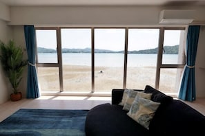 A room with a large window, a sofa, a potted plant, and a blue rug. - Lala Court Seaside Yagaji (Nago)